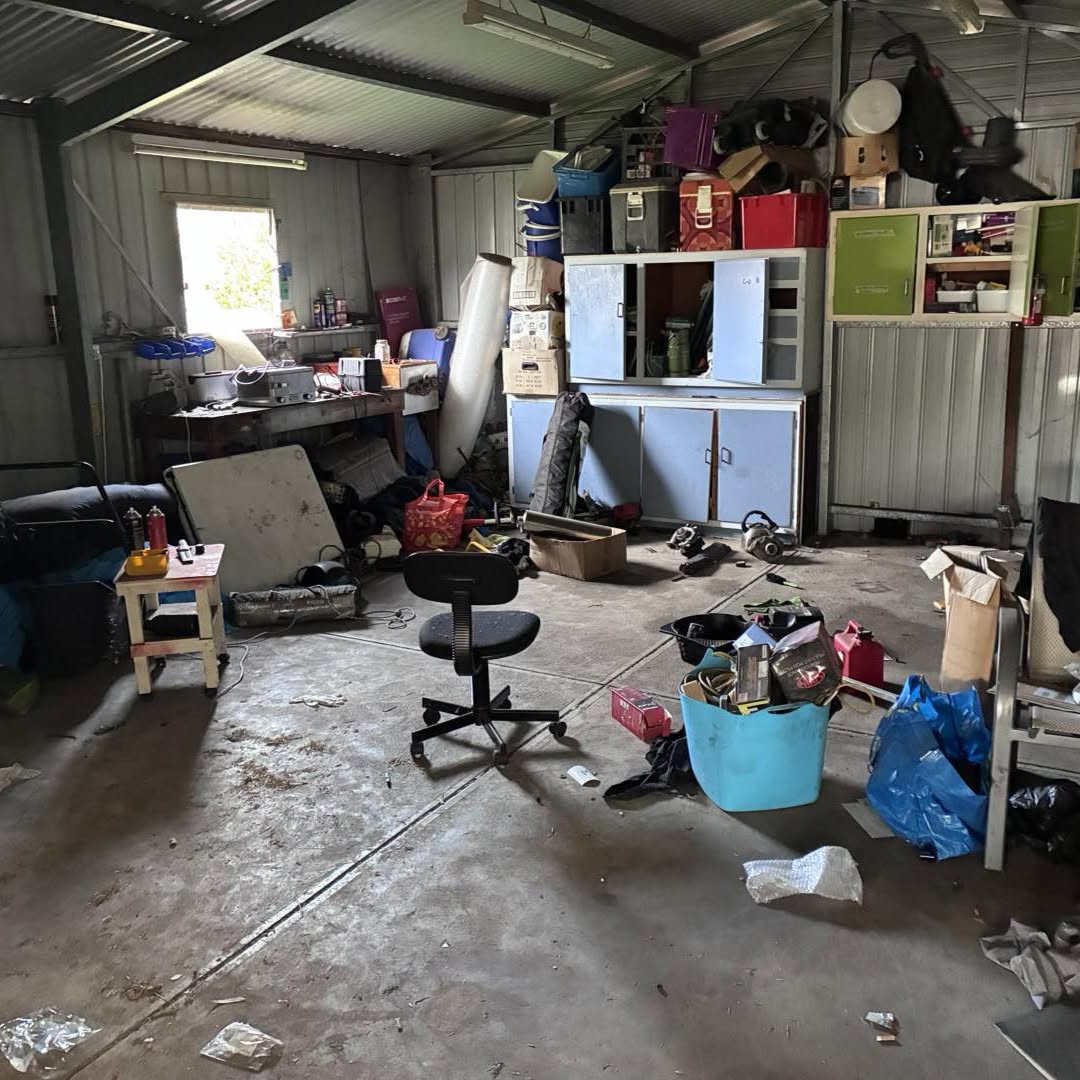 Shed packed with boxes, an office chair, tubs and loose rubbish before the clear out
