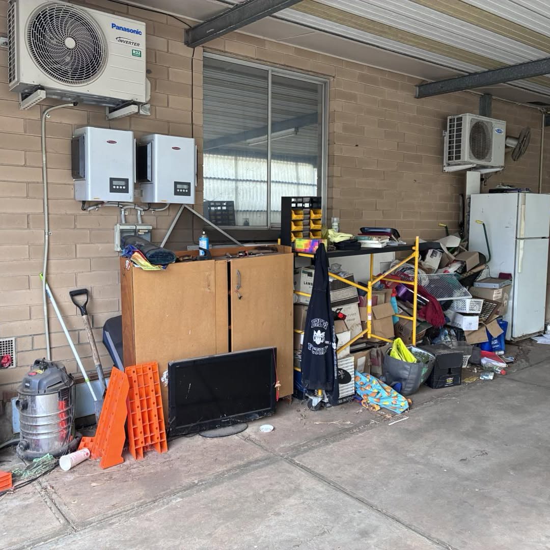 A carport stacked with cupboards, a television, a vacuum, boxes and a fridge before removal